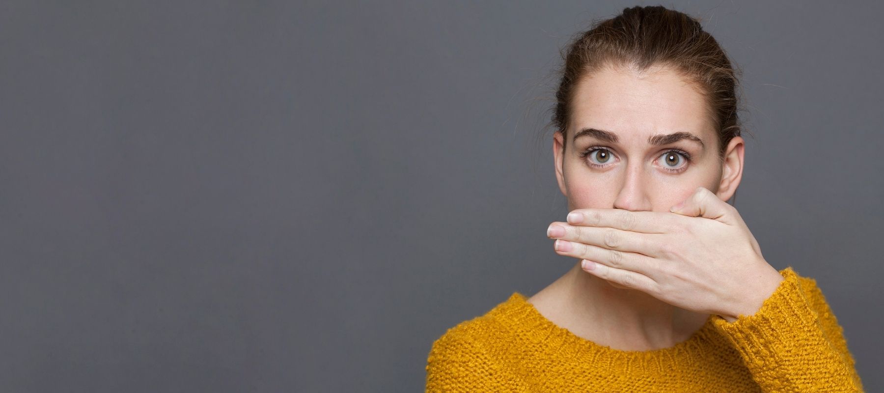 Woman wearing a yellow shirt covering her mouth to protect herself from bad breath